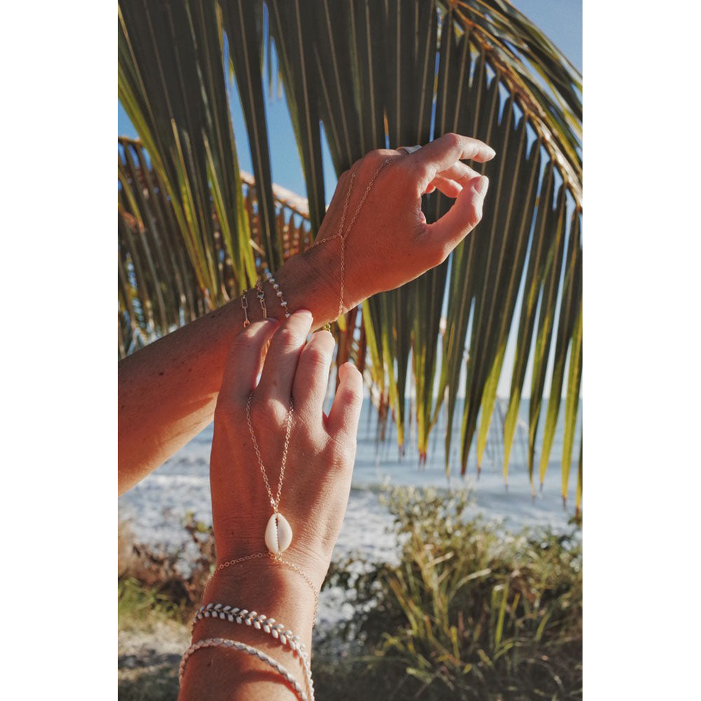 The cowrie shell handchain layered with a few other bracelets from Chains by Lauren.